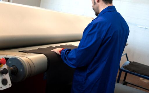 Artigiano in camice blu che lavora la pelle su un macchinario industriale in conceria
